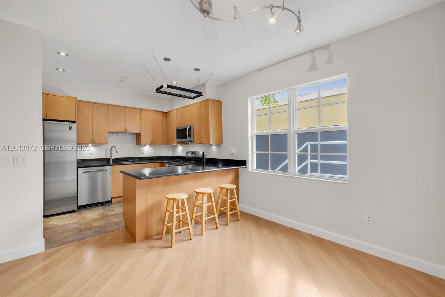 A kitchen features light wood cabinets, black countertops, stainless steel appliances, and three bar stools — 305 Jefferson Ave # 2, Miami Beach FL 33139, MIAMI BEACH, FL