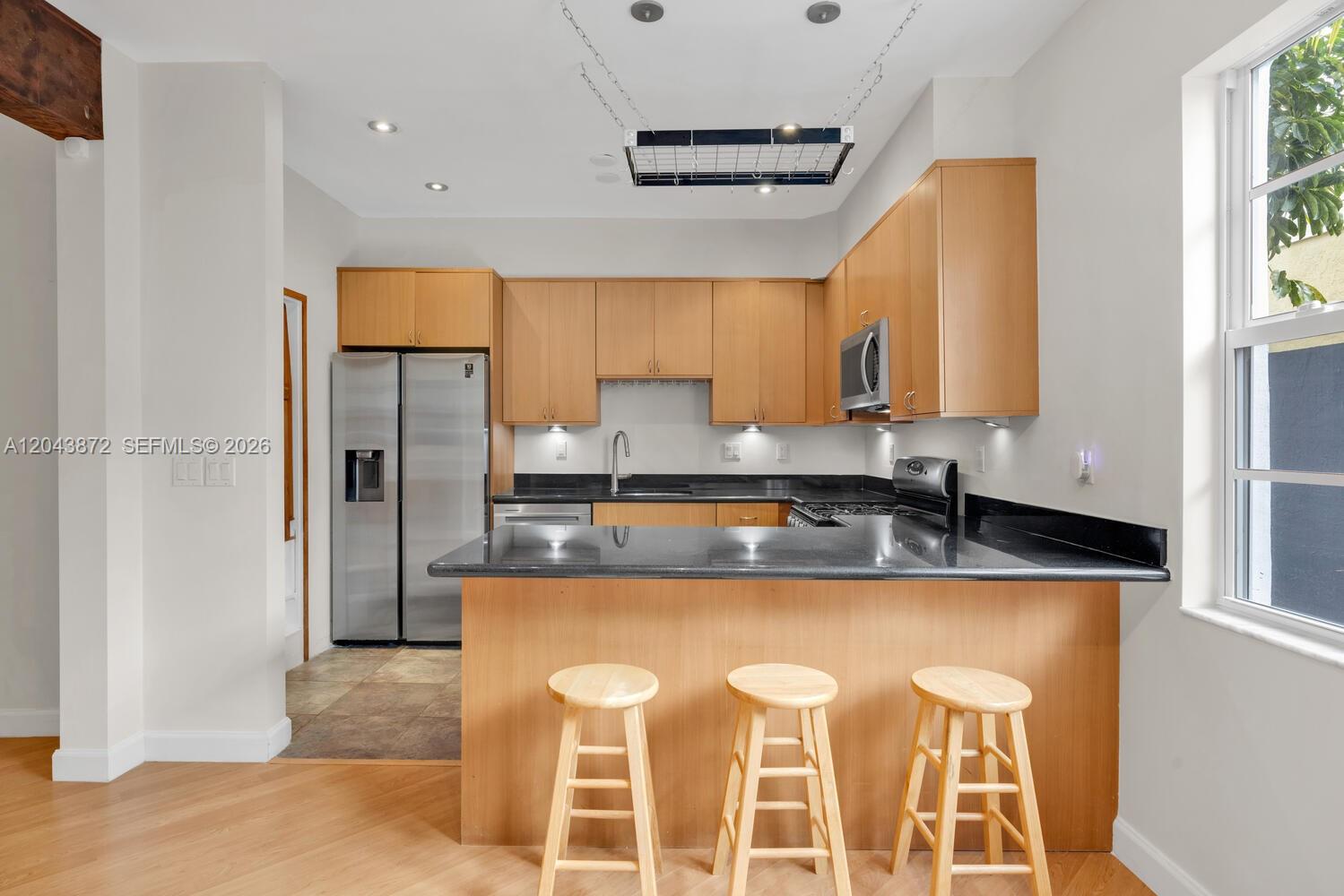 A kitchen features light wood cabinets, black countertops, a breakfast bar with stools, and stainless appliances — 305 Jefferson Ave # 2, Miami Beach FL 33139, MIAMI BEACH, FL