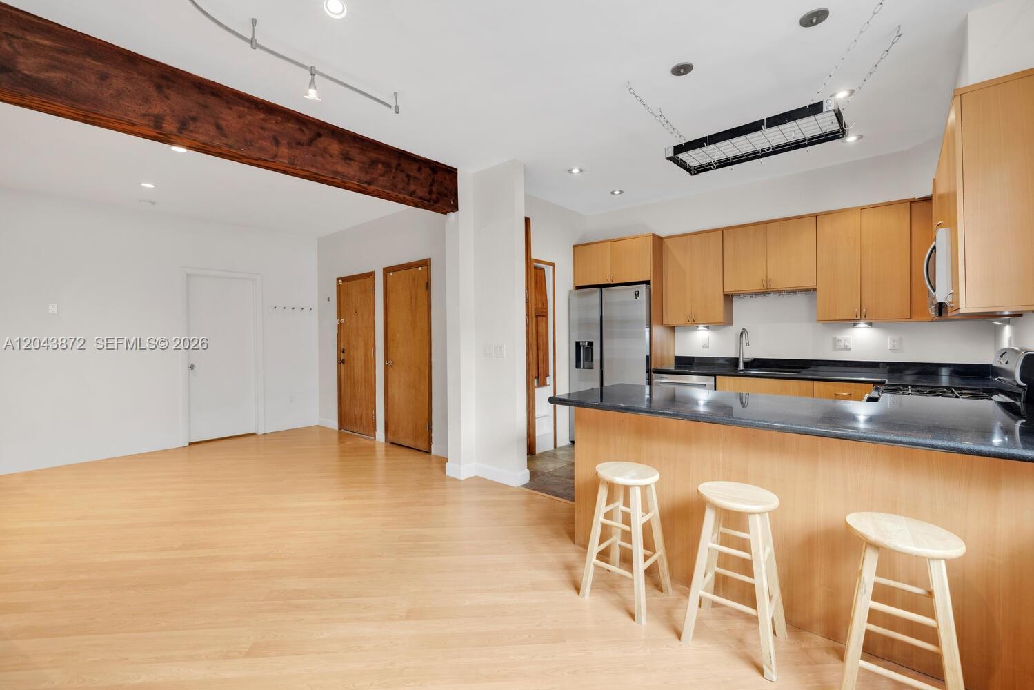 A kitchen with light wood cabinets and a black countertop opens to a living area — 305 Jefferson Ave # 2, Miami Beach FL 33139, MIAMI BEACH, FL