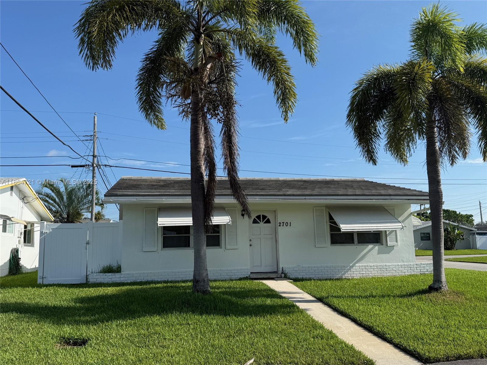 A single-story white house features a front walkway, two palm trees, and metal window awnings — 2701 NW 52nd Ct, Tamarac FL 33309, TAMARAC, FL