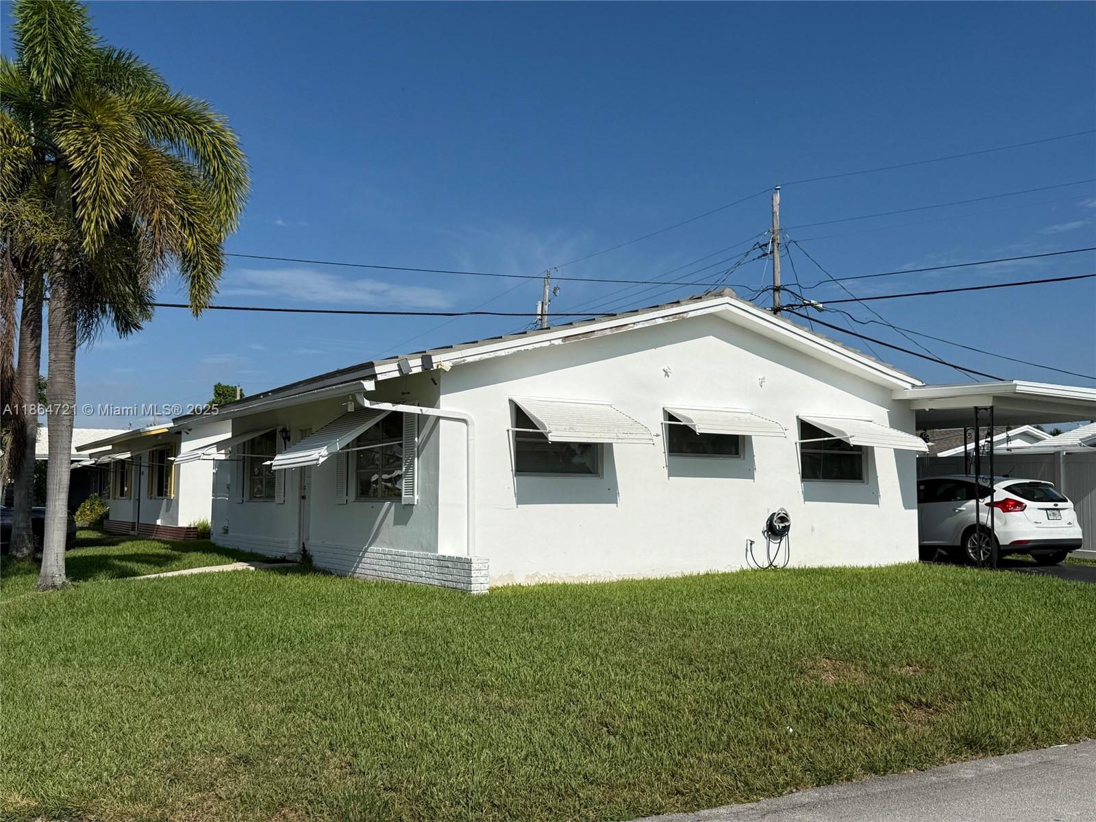 A white single-story house with metal awnings and a carport sits on a grassy lawn — 2701 NW 52nd Ct, Tamarac FL 33309, TAMARAC, FL