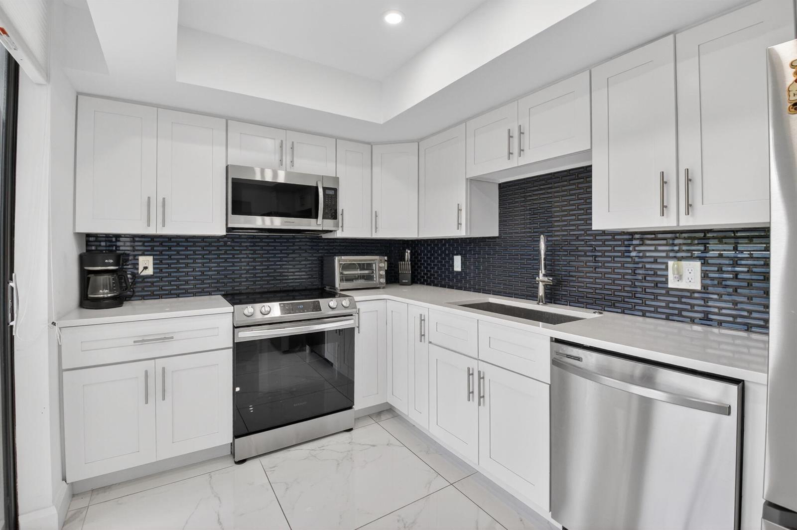 A kitchen with white cabinets, stainless steel appliances, quartz countertops, and a dark blue backsplash — 6815 Willow Wood Drive # 4012, Boca Raton FL 33434, BOCA RATON, FL