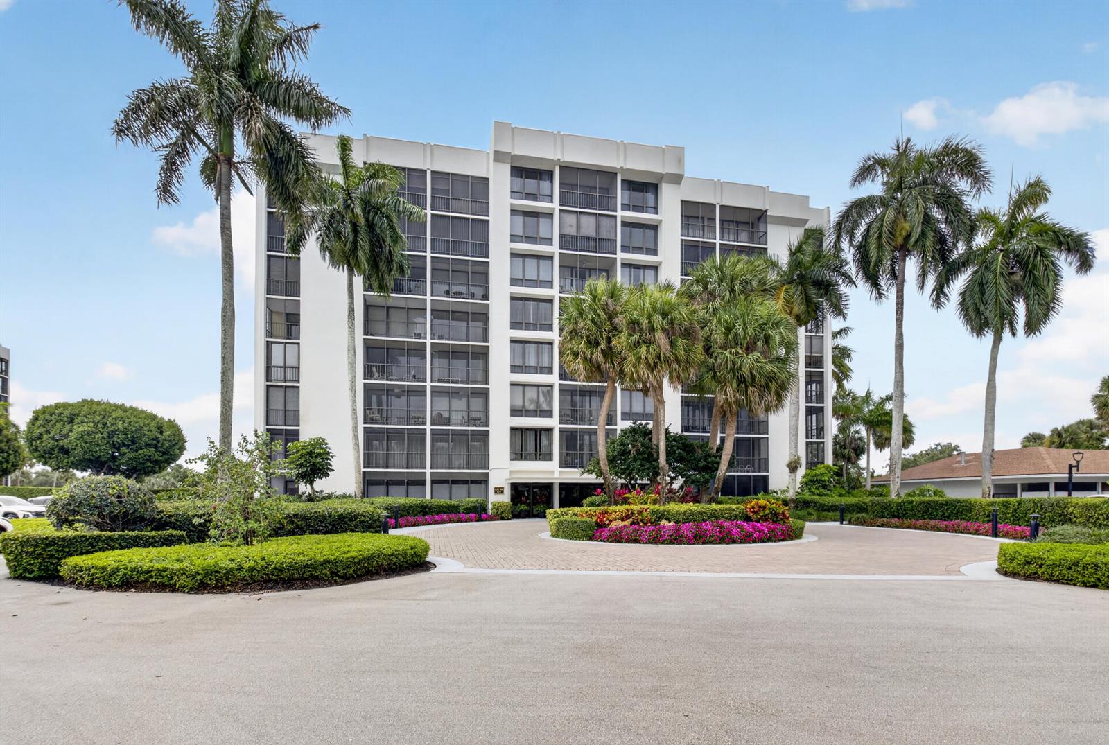 A multi-story white apartment building features screened balconies, palm trees, and a circular driveway — 6815 Willow Wood Drive # 4012, Boca Raton FL 33434, BOCA RATON, FL