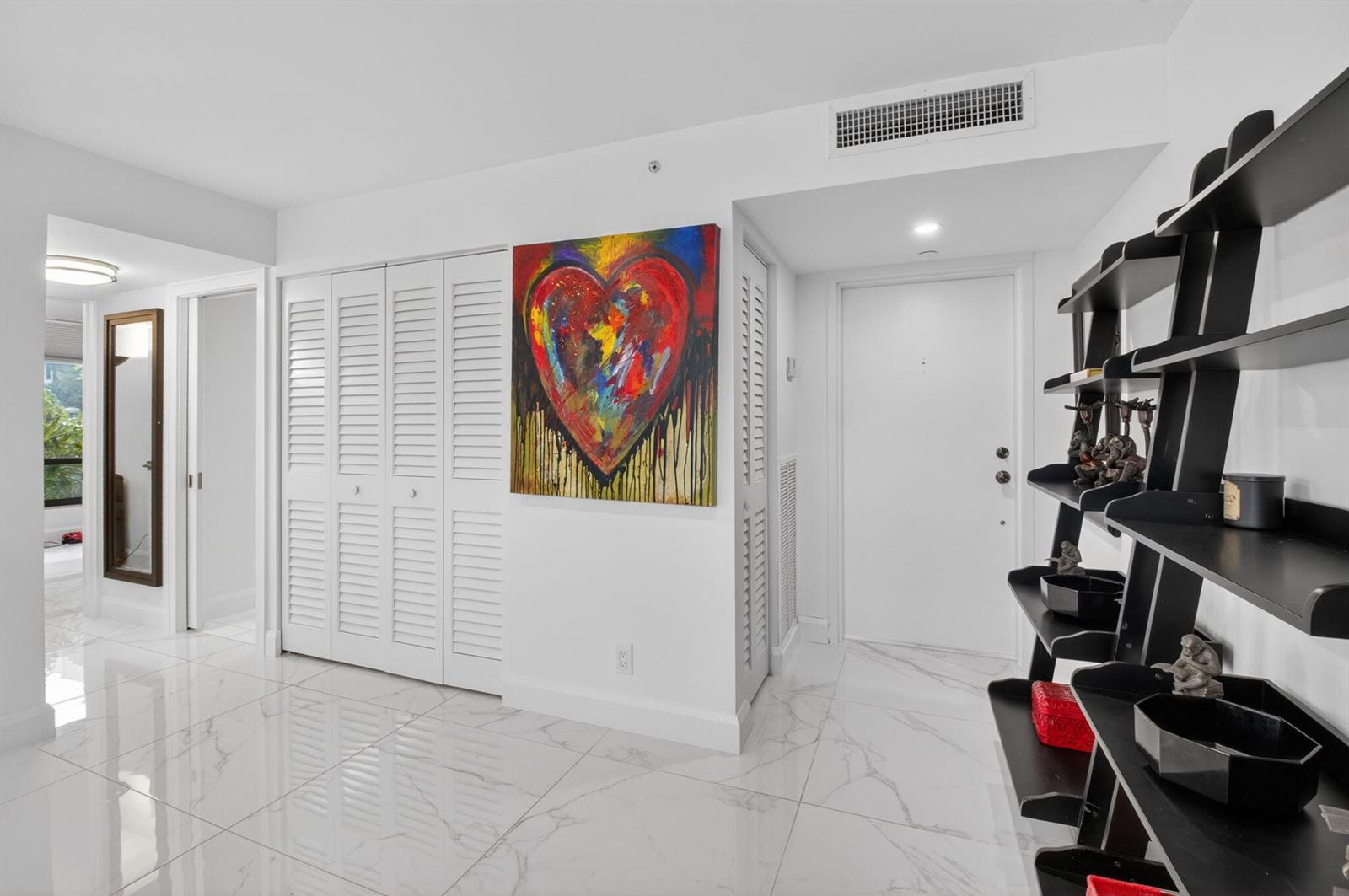 An entryway with white marble floors, a heart painting, louvered closet doors, and black shelving — 6815 Willow Wood Drive # 4012, Boca Raton FL 33434, BOCA RATON, FL