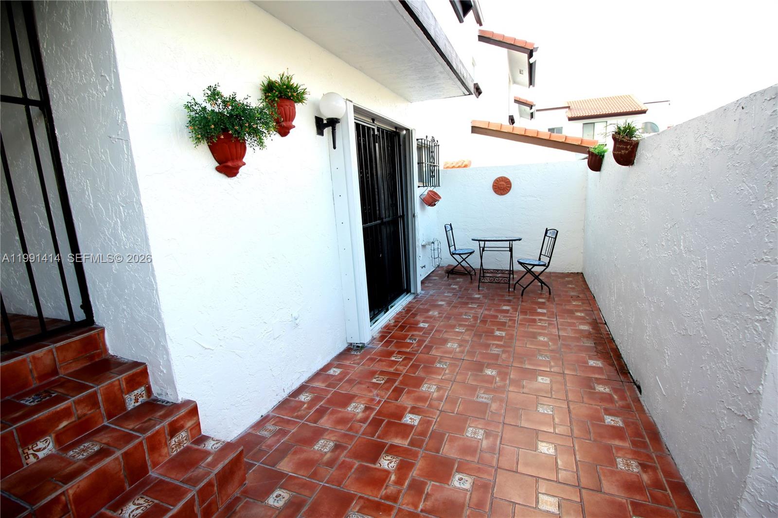 A tiled patio features a small bistro set, wall-mounted planters, and steps leading upward — 1221 SW 124th Ct, Miami FL 33184, MIAMI, FL
