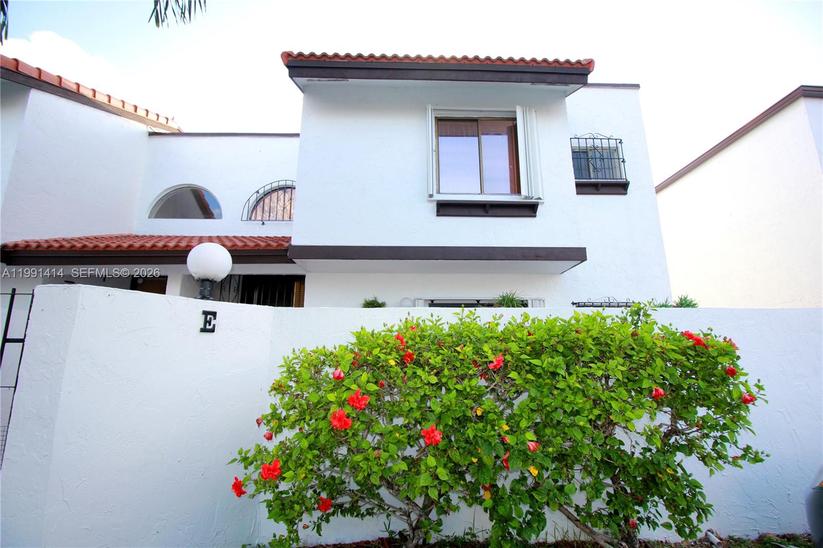 A white two-story building features a red tile roof and a flowering hibiscus bush — 1221 SW 124th Ct, Miami FL 33184, MIAMI, FL