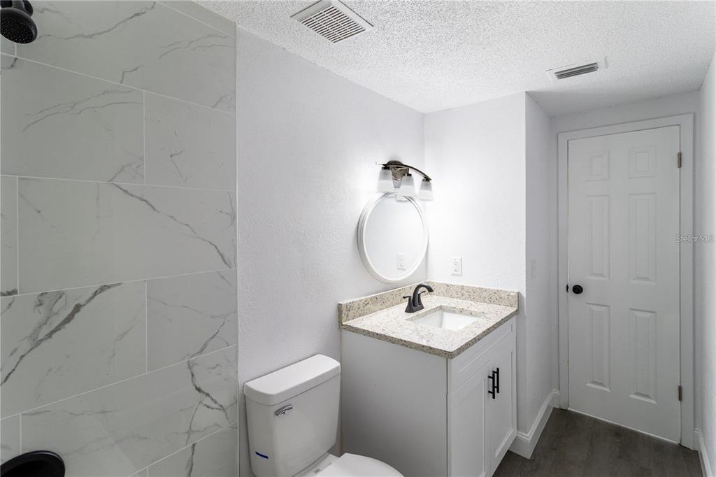 A bathroom features a white vanity with a granite countertop, a toilet, and a tiled shower — 3432 DANNY BRYAN BOULEVARD, TAMPA, FL