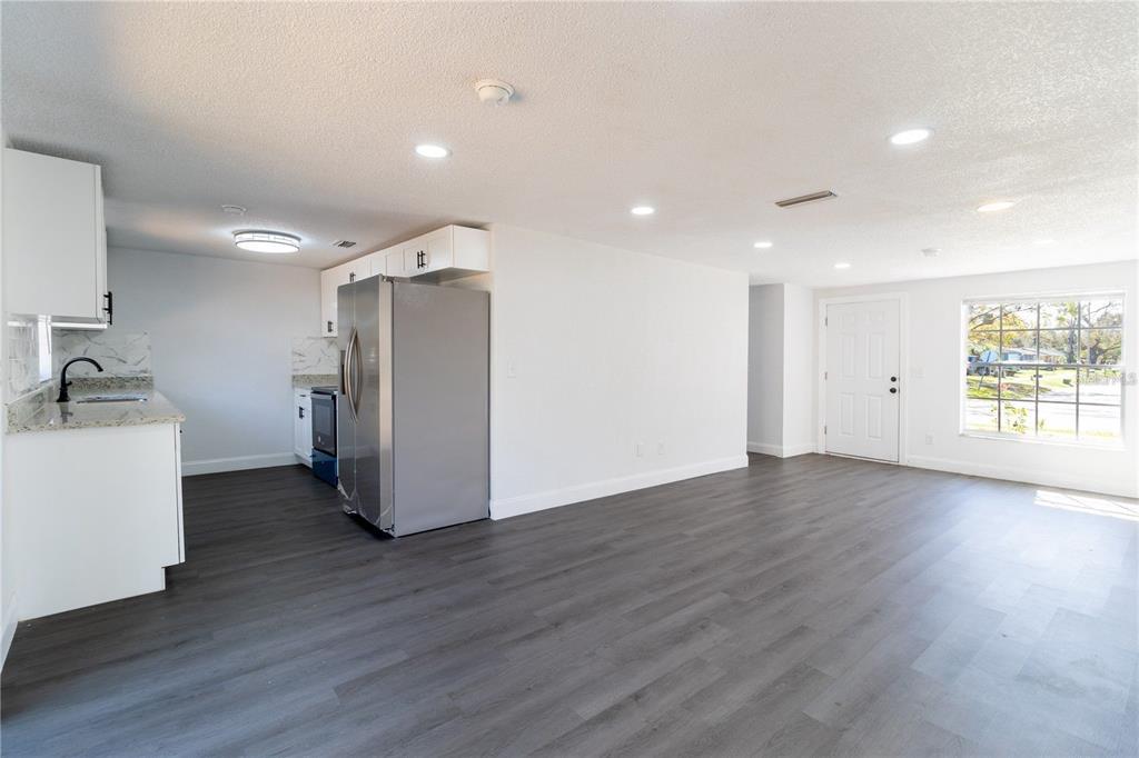 An open-concept kitchen and living area features white cabinets, stainless steel appliances, and dark flooring — 3432 DANNY BRYAN BOULEVARD, TAMPA, FL