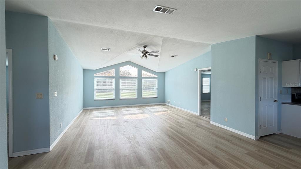 A spacious living room features light blue walls, vaulted ceilings, and light wood-look flooring — 1831 WINCHESTER COURT S, ST CLOUD, FL
