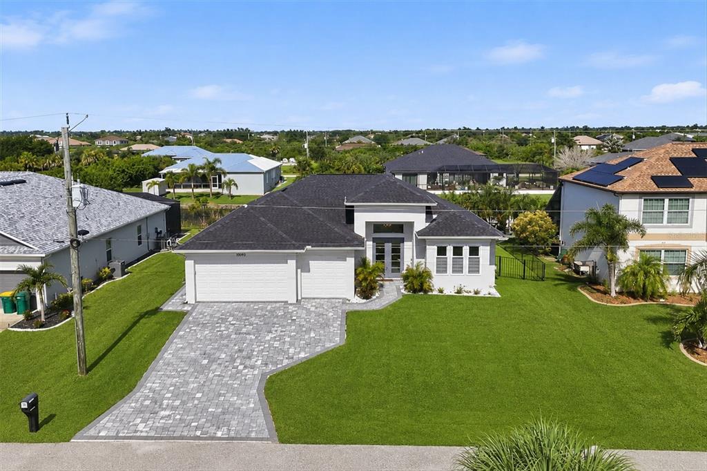 An aerial view shows a single-story house with a gray roof, white exterior, and paver driveway — 10099 LONG BRANCH STREET, PORT CHARLOTTE, FL