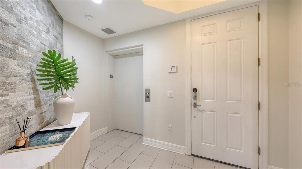 An entryway features a white door, a private elevator, a stone accent wall, and tile flooring — 1921 MONTE CARLO DRIVE UNIT 302, SARASOTA, FL