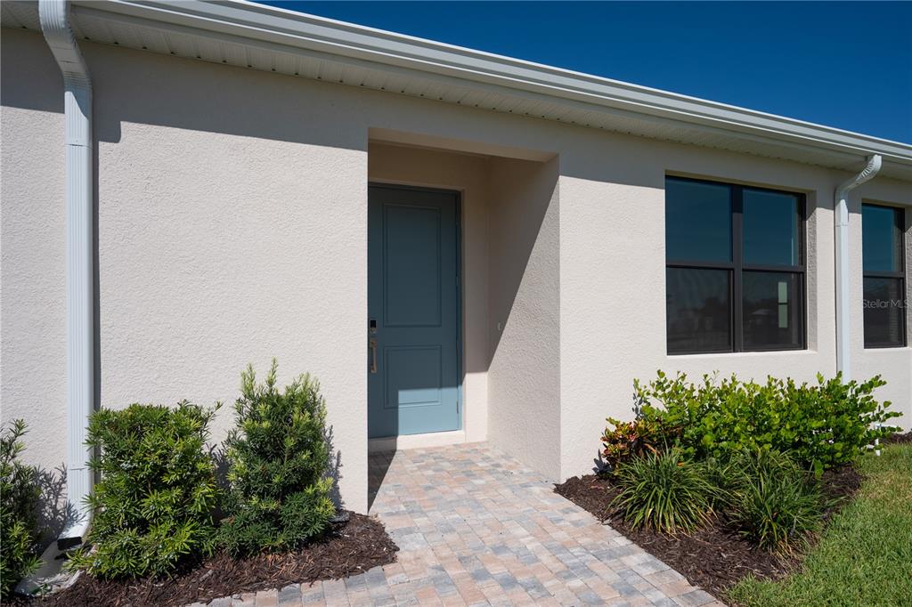A light-colored stucco house exterior features a blue front door and a paved walkway — 5890 WINDBREAK COURT, APOLLO BEACH, FL