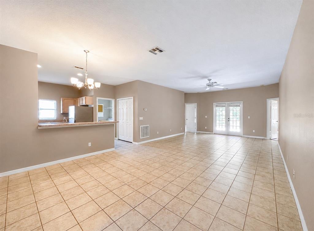 An open-concept living and dining area features beige tile flooring, neutral walls, and a kitchen — 336 MAGICAL WAY, KISSIMMEE, FL