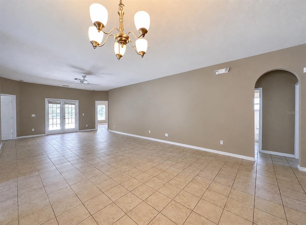 A large, empty room with beige walls, tile flooring, a chandelier, and an arched doorway — 336 MAGICAL WAY, KISSIMMEE, FL