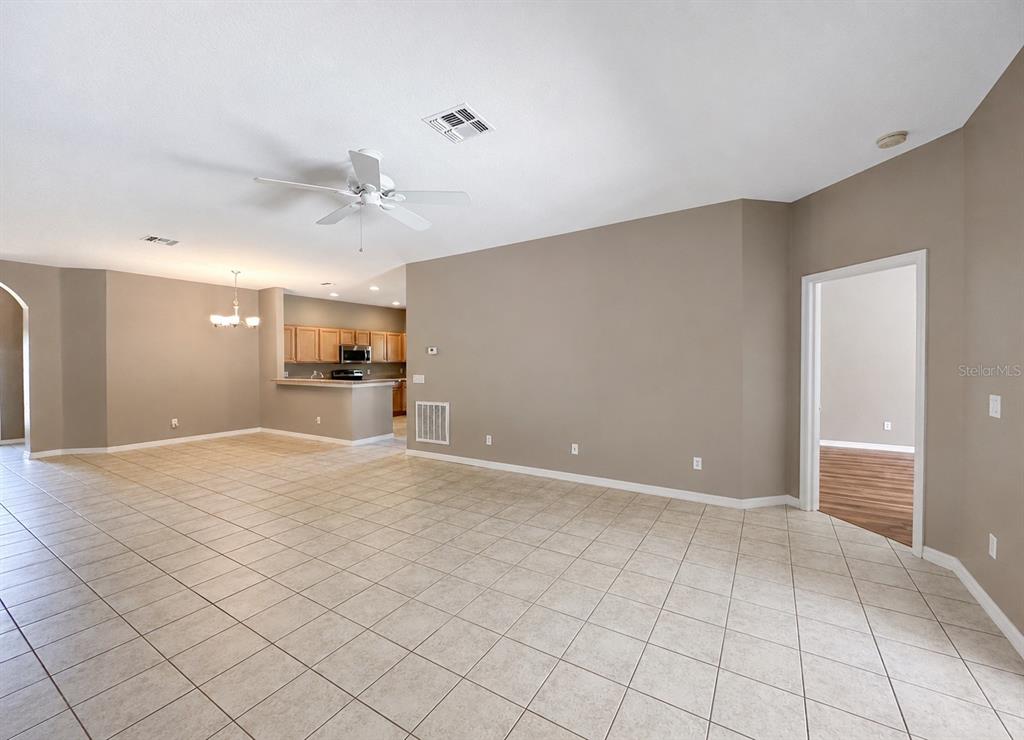 An open-concept living area features beige tile flooring, neutral walls, and a kitchen with cabinets — 336 MAGICAL WAY, KISSIMMEE, FL