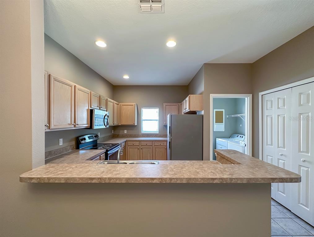 A kitchen features light wood cabinets, laminate countertops, stainless steel appliances, and a breakfast bar — 336 MAGICAL WAY, KISSIMMEE, FL