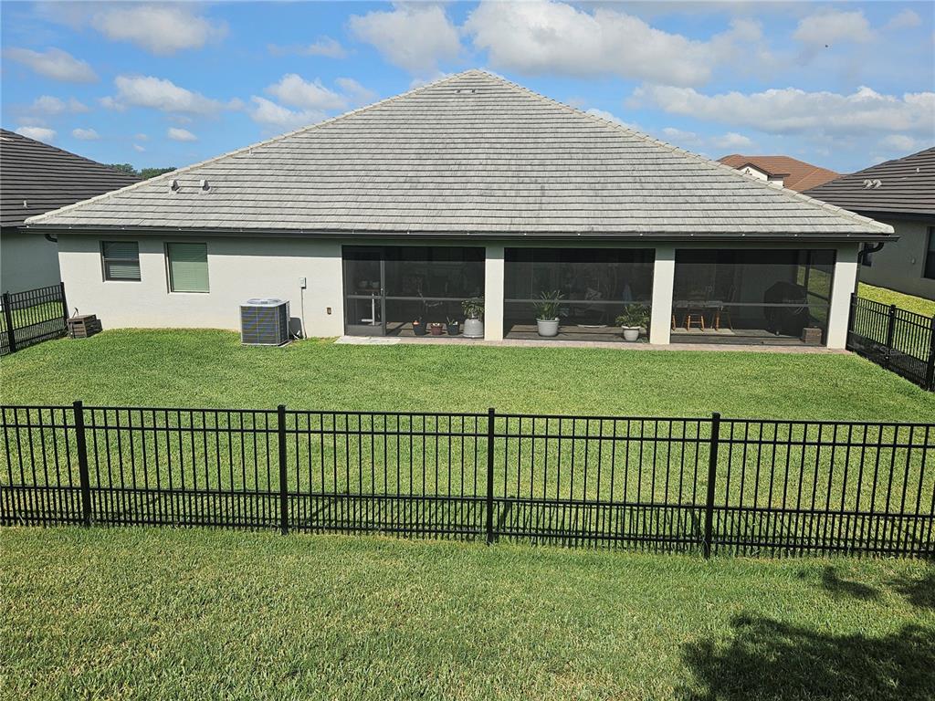 The rear exterior of a house features a screened-in patio, a fenced yard, and a roof — 4222 JULIANA LAKE DRIVE, AUBURNDALE, FL