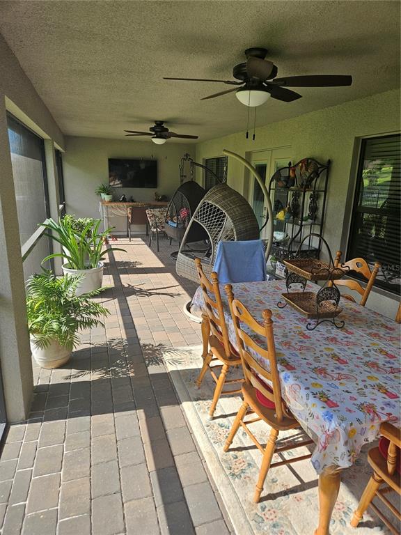 A covered patio features a dining table, hanging chairs, potted plants, and brick flooring — 4222 JULIANA LAKE DRIVE, AUBURNDALE, FL