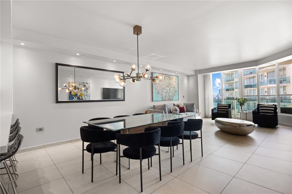 A dining area with a glass table, black chairs, and a modern chandelier near windows — 25 MUNOZ RIVERA UNIT 704, SAN JUAN, PR