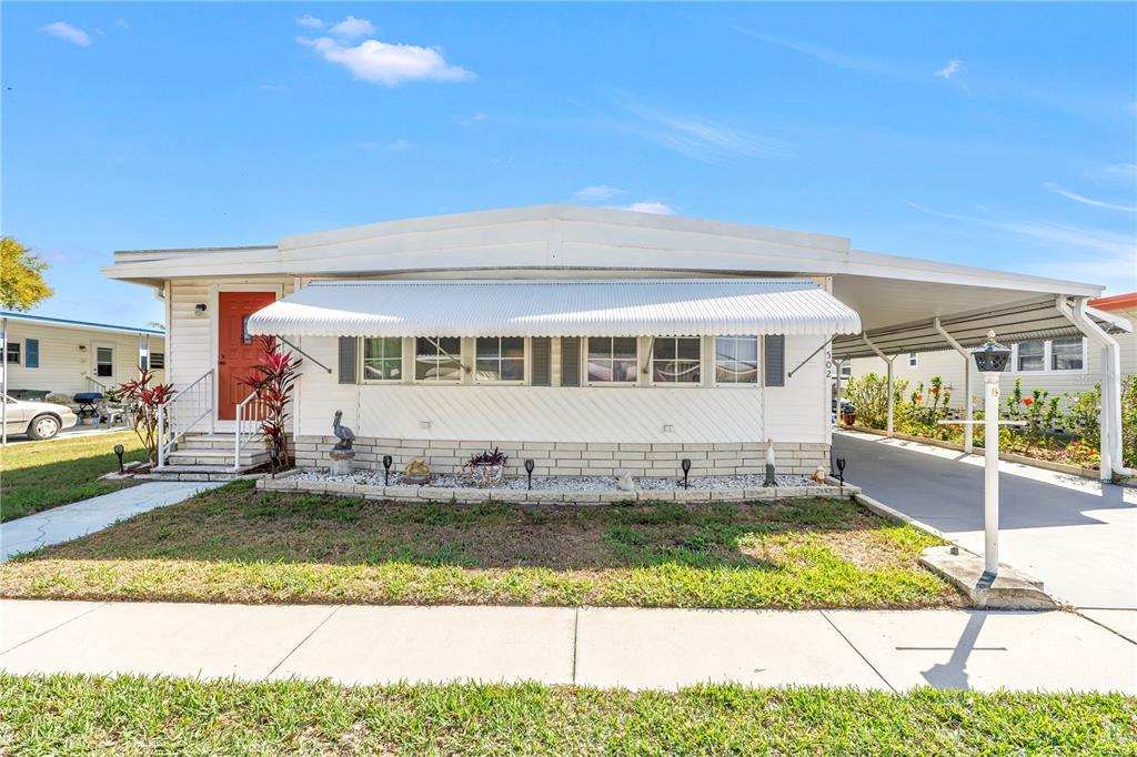 A white manufactured home with a carport, front awning, and a small landscaped garden bed — 1100 BELCHER ROAD S UNIT 502, LARGO, FL