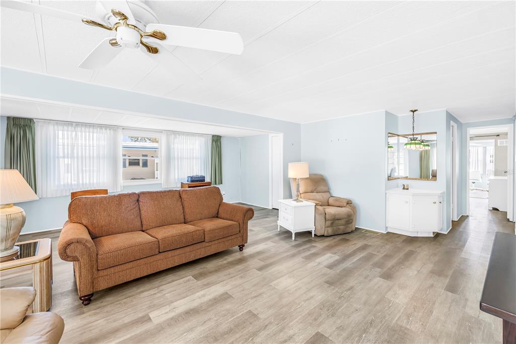 A living room features light blue walls, wood-look flooring, a brown sofa, and a ceiling fan — 1100 BELCHER ROAD S UNIT 502, LARGO, FL