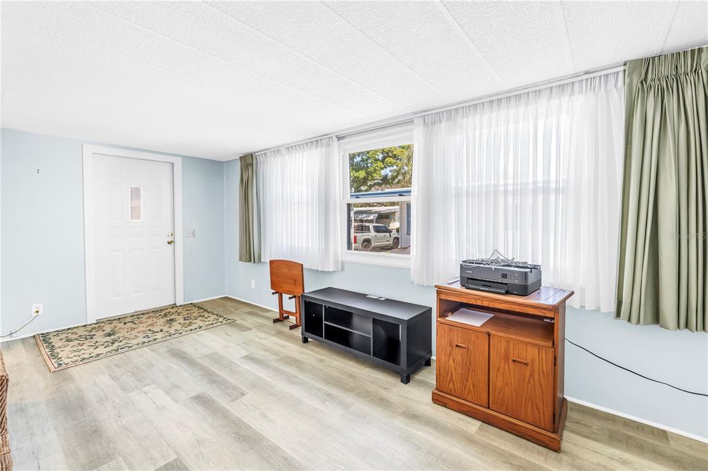 A living room with light blue walls, wood-look flooring, a white door, and large windows — 1100 BELCHER ROAD S UNIT 502, LARGO, FL