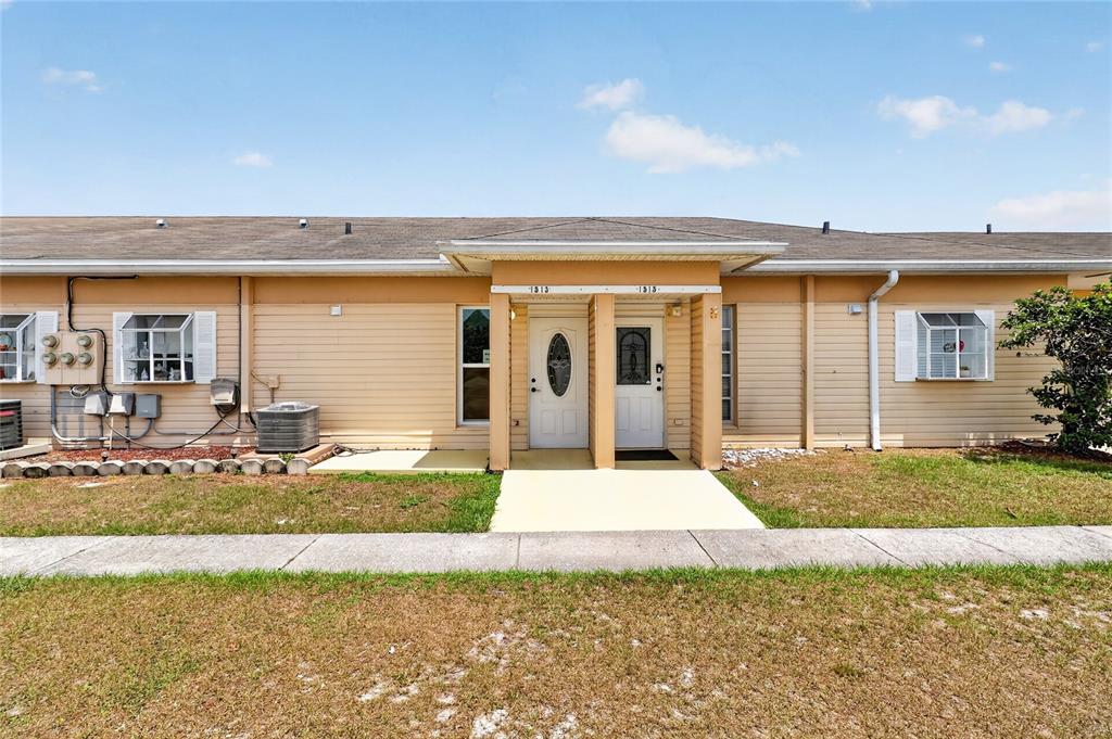 A single-story duplex with tan siding, two white front doors, and a shared covered entryway — 1513 CLUB CIRCLE, LAKESHORE, FL