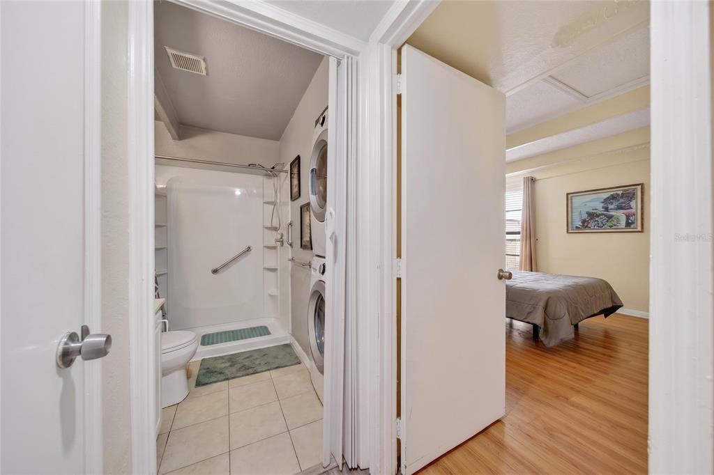 A bathroom with a shower and stacked laundry units sits beside a bedroom with wood flooring — 1513 CLUB CIRCLE, LAKESHORE, FL