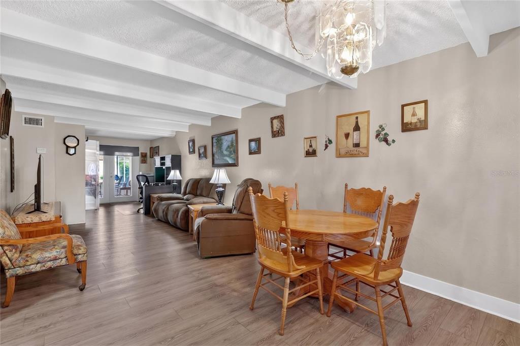 A living and dining area features wood-look flooring, white ceiling beams, and a chandelier — 1513 CLUB CIRCLE, LAKESHORE, FL