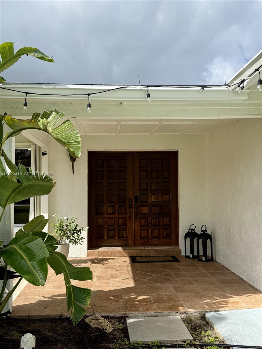 A covered entryway features double wooden doors, tiled flooring, and string lights — 625 Whippoorwill Ter, West Palm Beach FL 33411, WEST PALM BEACH, FL