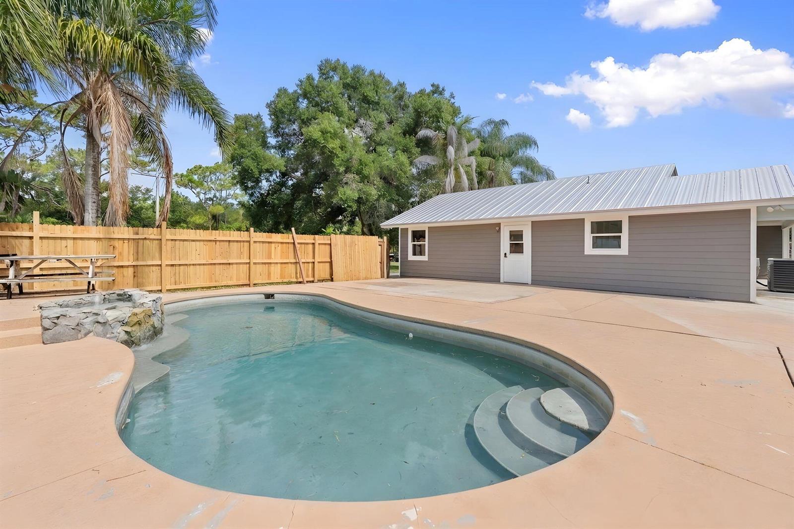 A backyard features a swimming pool with a stone water feature and a wooden fence — 202 Laidback Way, Fort Pierce FL 34945, FORT PIERCE, FL