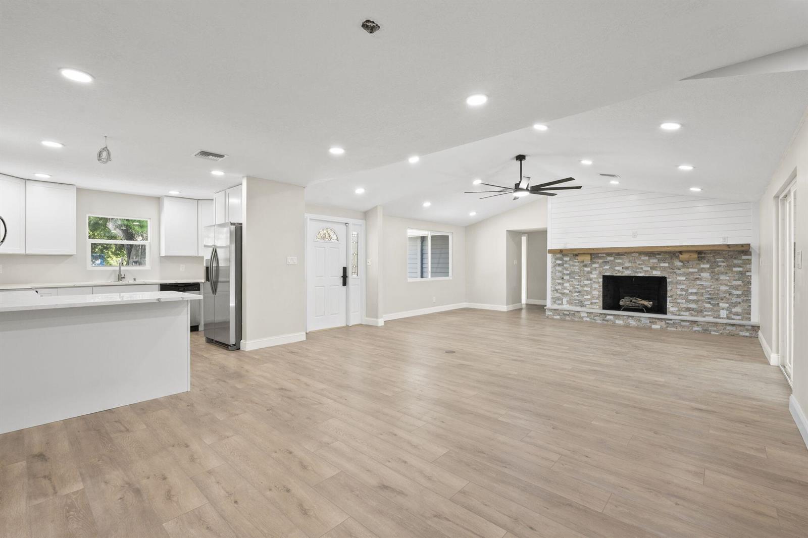 An open-concept living room and kitchen featuring light wood flooring, recessed lighting, and a fireplace — 202 Laidback Way, Fort Pierce FL 34945, FORT PIERCE, FL