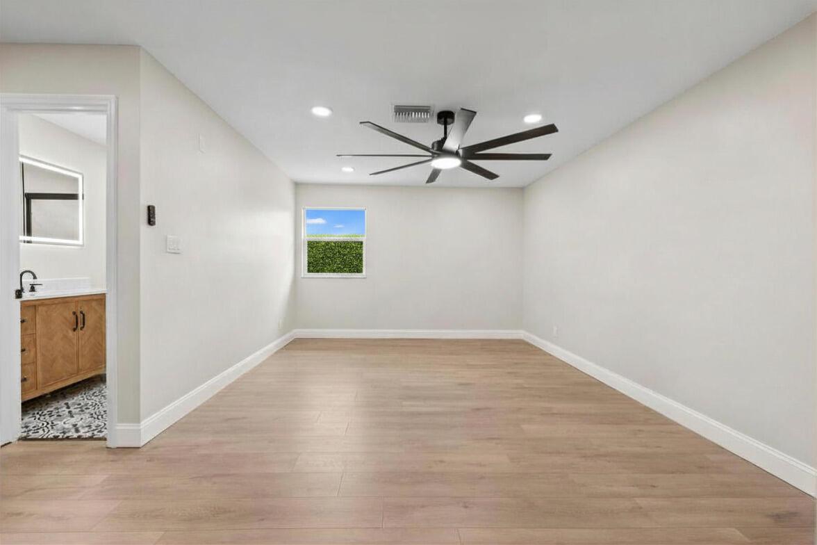 A bedroom with light wood-look flooring, white walls, a ceiling fan, and an attached bathroom — 202 Laidback Way, Fort Pierce FL 34945, FORT PIERCE, FL