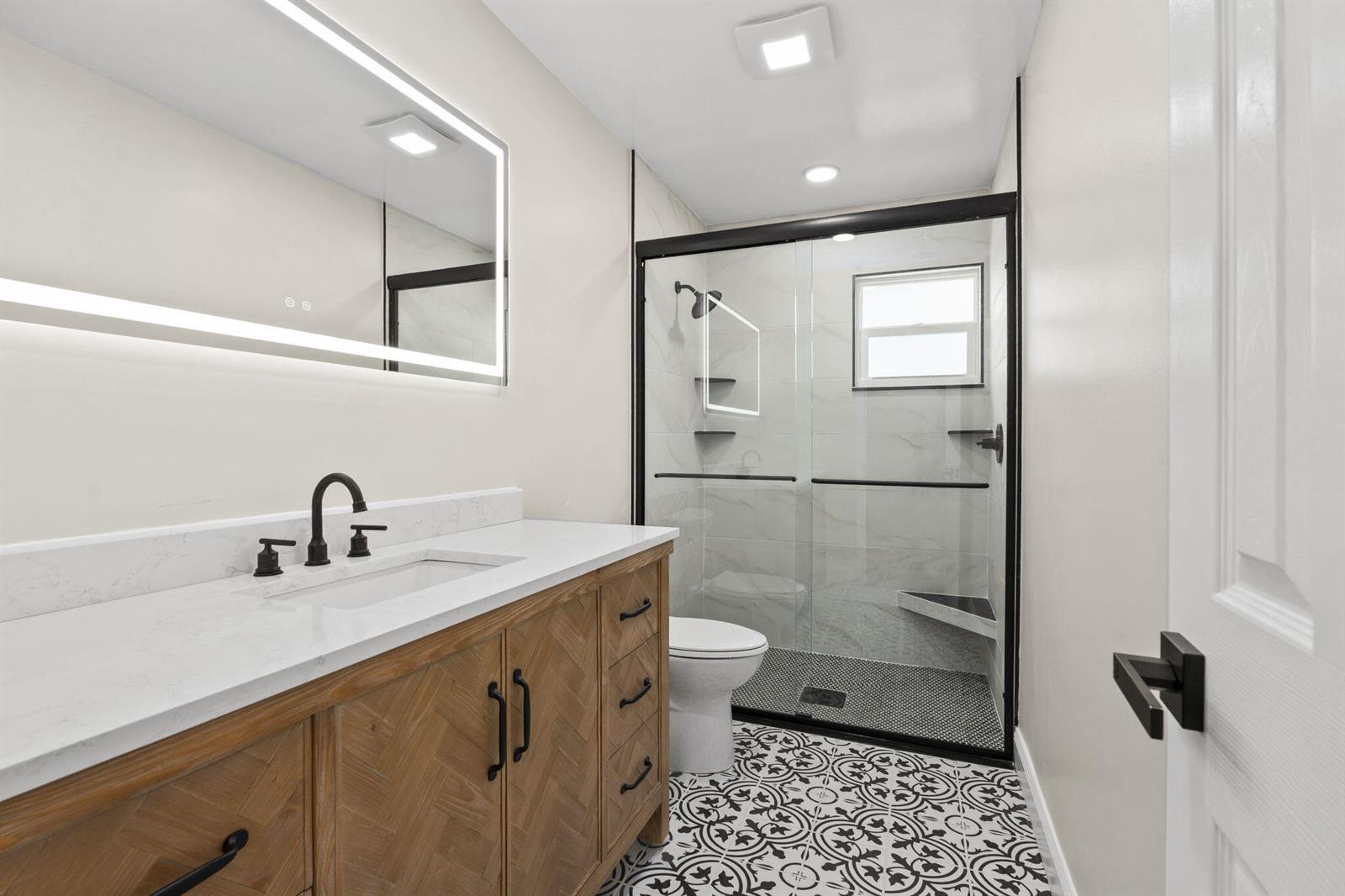A bathroom features a wooden vanity, a walk-in glass shower, and patterned floor tiles — 202 Laidback Way, Fort Pierce FL 34945, FORT PIERCE, FL