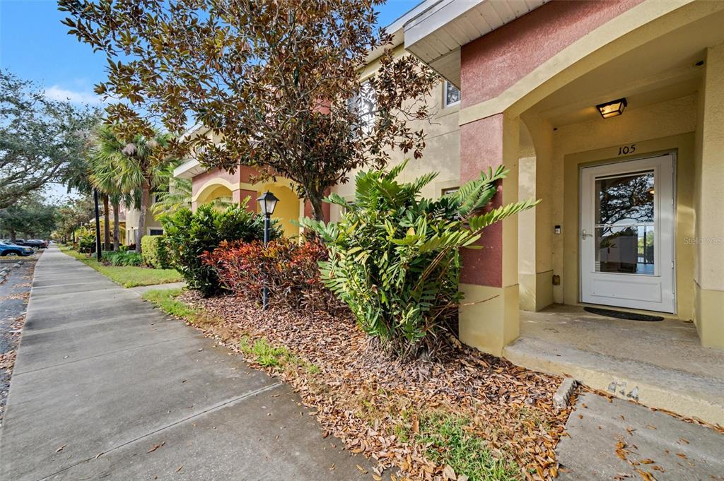 A sidewalk leads to the entrance of a building with a white door labeled 105 — 3505 45TH TERRACE W UNIT 105, BRADENTON, FL