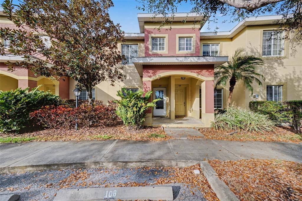 A two-story townhouse exterior features a covered entryway, tan and red stucco, and landscaping — 3505 45TH TERRACE W UNIT 105, BRADENTON, FL