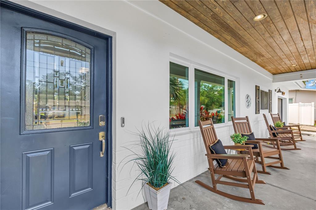 A covered porch features a dark blue front door, white brick walls, and wooden rocking chairs — 10819 SEMINOLE DRIVE N, ST PETERSBURG, FL