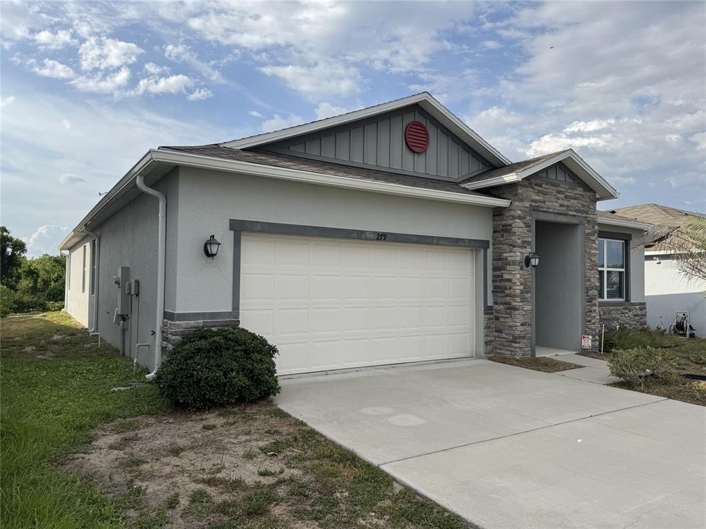 A single-story house features a two-car garage, stone accents, and a gray stucco exterior — 279 SUNFISH DRIVE DRIVE, WINTER HAVEN, FL