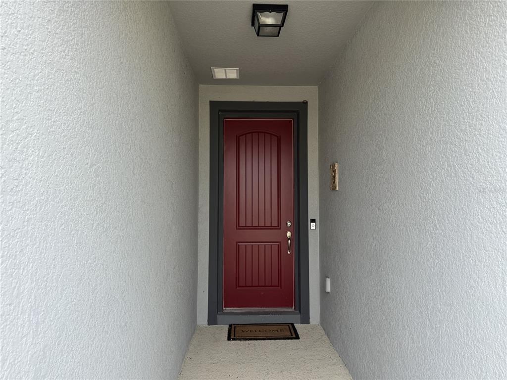A red front door is set within a recessed entryway with gray stucco walls — 279 SUNFISH DRIVE DRIVE, WINTER HAVEN, FL