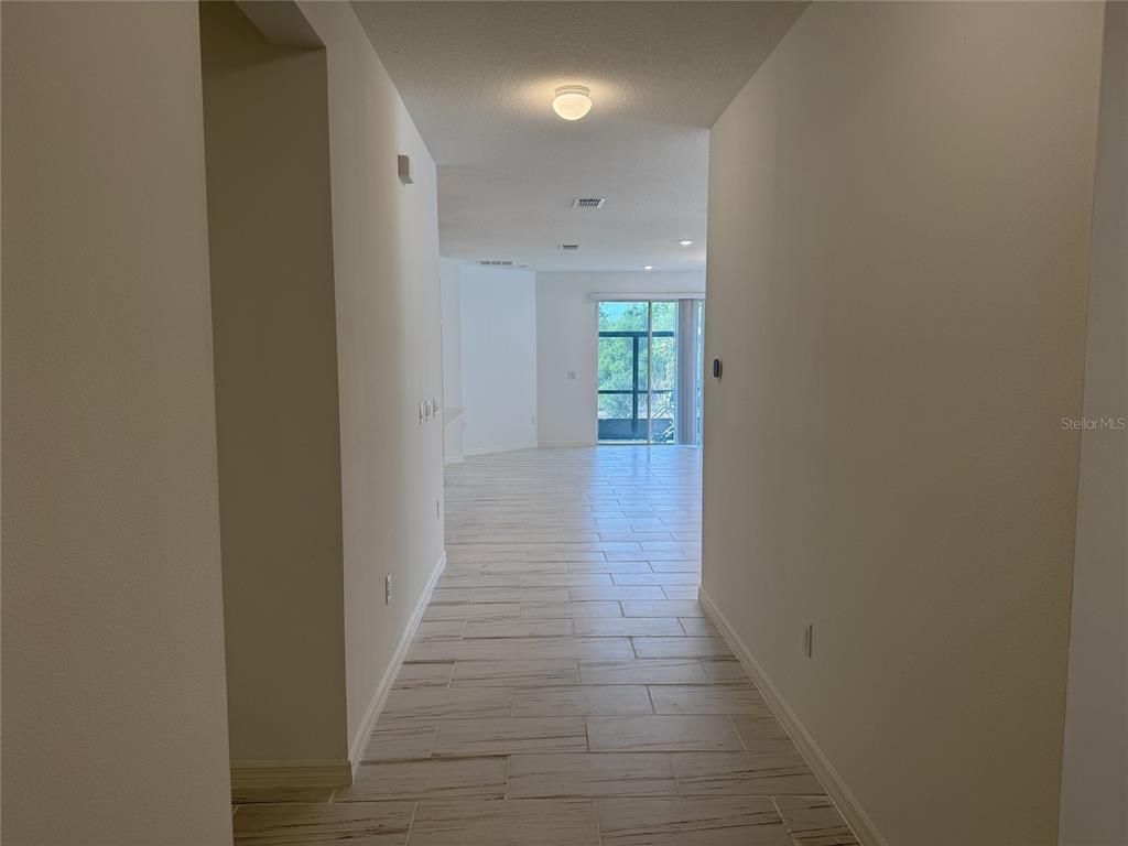 A hallway with light-colored tile flooring leads toward an open living area with sliding glass doors — 279 SUNFISH DRIVE DRIVE, WINTER HAVEN, FL