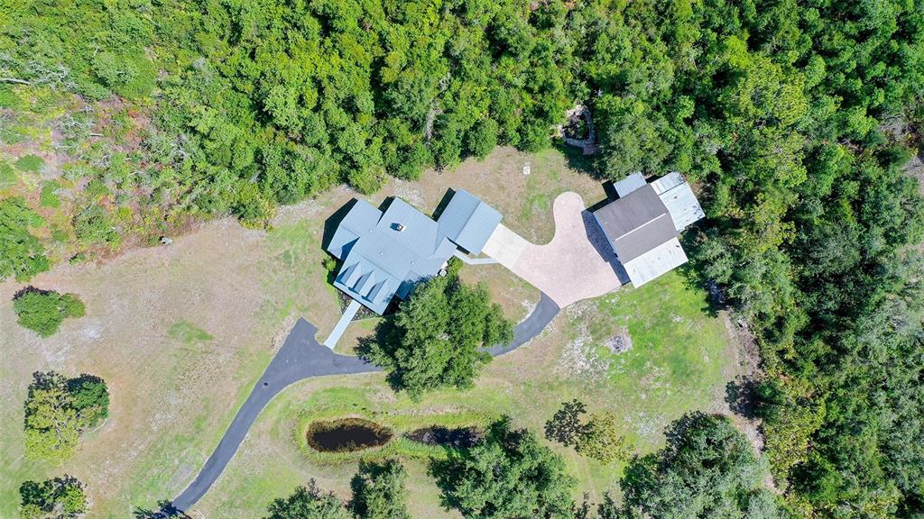 An aerial view shows a house with a metal roof, driveway, and pond amidst trees — 28401 104TH DR E, MYAKKA CITY, FL