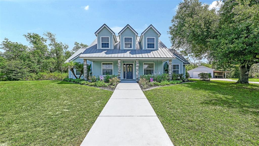 A light blue house with a metal roof and three dormers features a concrete walkway — 28401 104TH DR E, MYAKKA CITY, FL