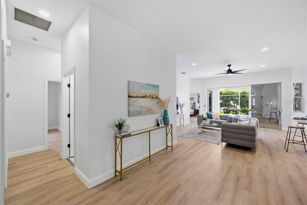 A bright, open-concept living area features light wood flooring, a gold console table, and furniture — 6011 CHAPARRAL AVENUE, SARASOTA, FL
