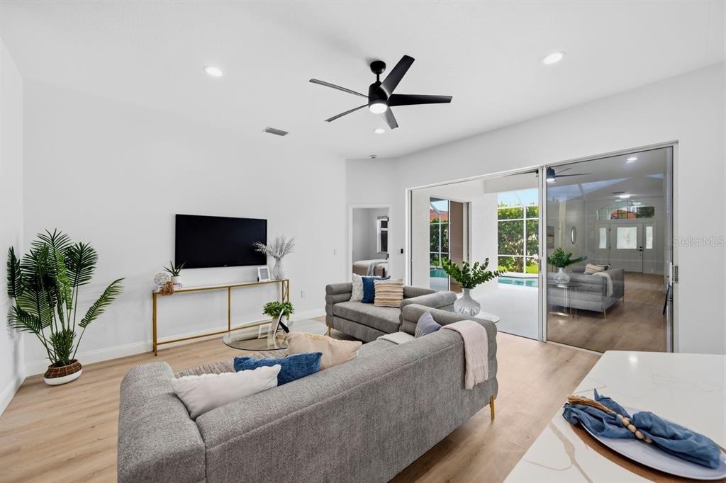 A bright living room features gray sectional sofas, a wall-mounted television, and sliding glass doors — 6011 CHAPARRAL AVENUE, SARASOTA, FL