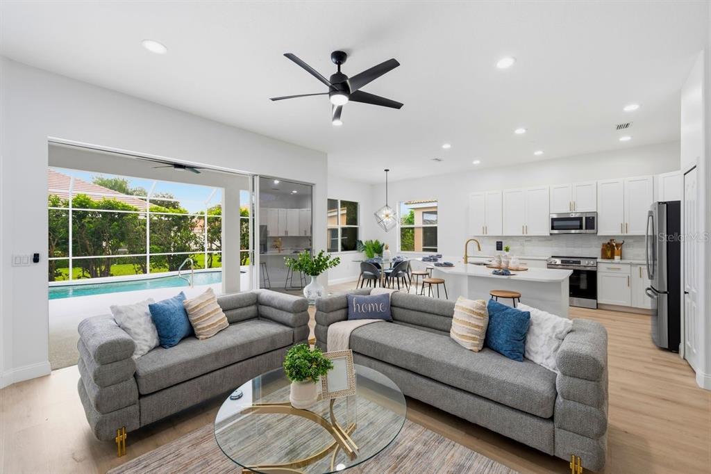 An open-concept living room and kitchen feature gray sofas, a pool view, and white cabinetry — 6011 CHAPARRAL AVENUE, SARASOTA, FL