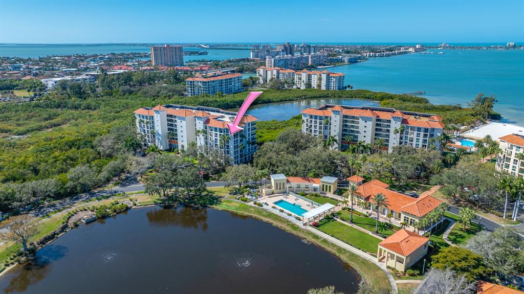 An aerial view shows a multi-story apartment building with a pool and a lake — 4750 DOLPHIN CAY LANE S UNIT 509, ST PETERSBURG, FL