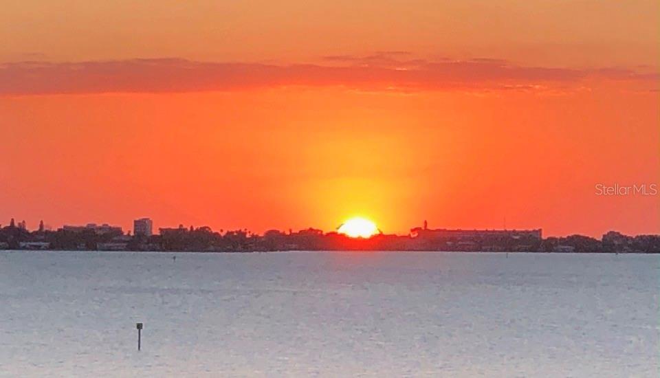 A vibrant orange sunset glows over a distant city skyline across a calm body of water — 4750 DOLPHIN CAY LANE S UNIT 509, ST PETERSBURG, FL