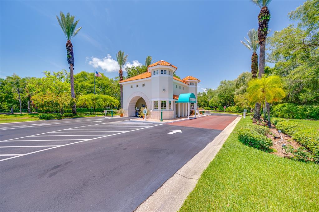 An exterior view of a gated community entrance with a guardhouse and palm trees — 4750 DOLPHIN CAY LANE S UNIT 509, ST PETERSBURG, FL