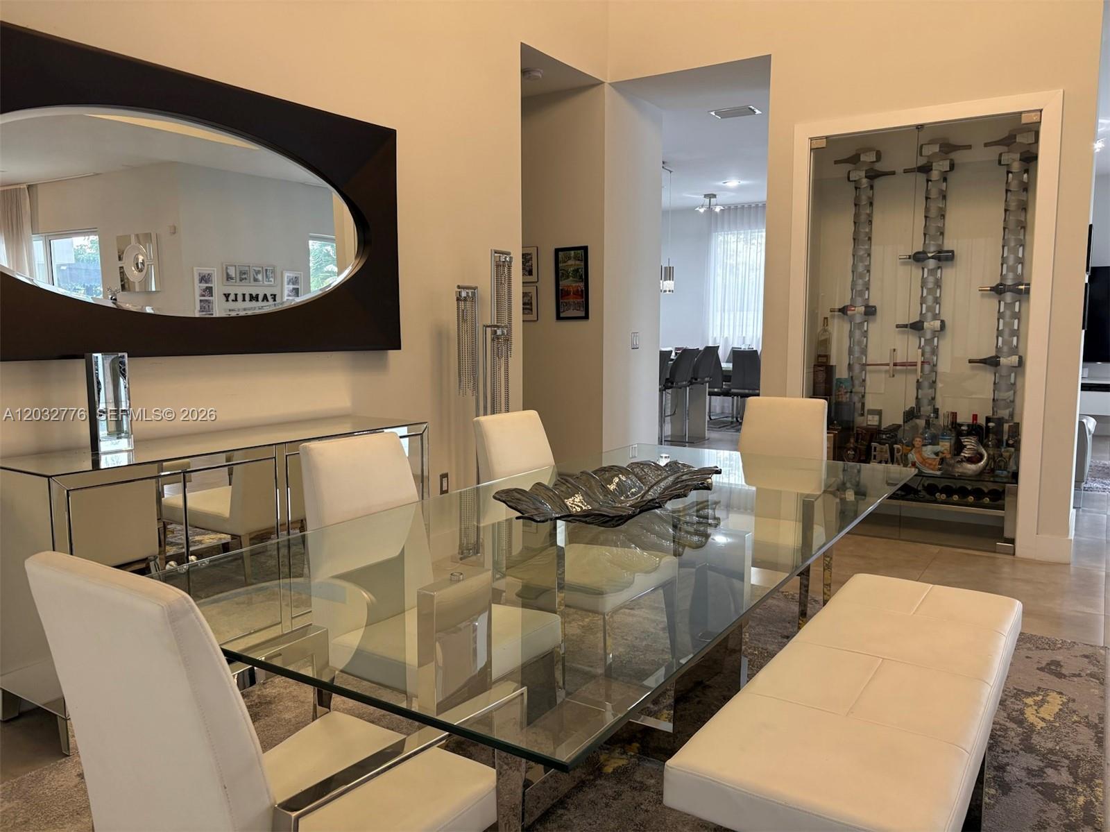 A modern dining room features a glass table, white chairs, a mirrored sideboard, and a wine display — 7433 NW 99th Ave, Doral FL 33178, DORAL, FL