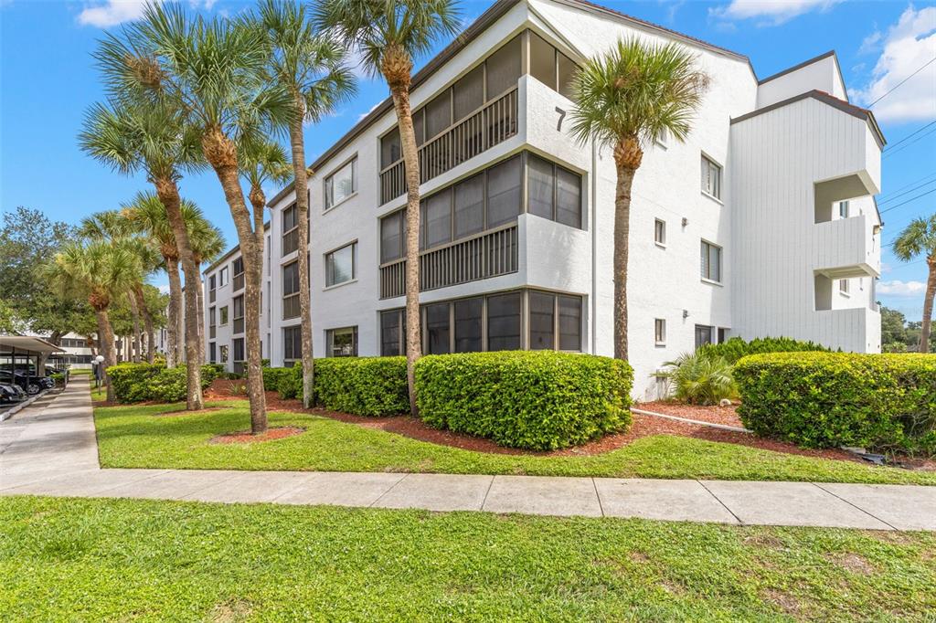 A three-story white apartment building with screened balconies and palm trees in the foreground — 2593 COUNTRYSIDE BOULEVARD UNIT 7304, CLEARWATER, FL
